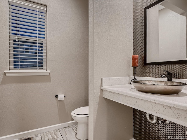 bathroom featuring backsplash, baseboards, toilet, a textured wall, and a sink