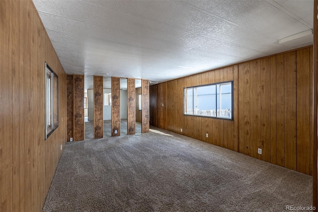 unfurnished room with a textured ceiling, wood walls, and carpet flooring