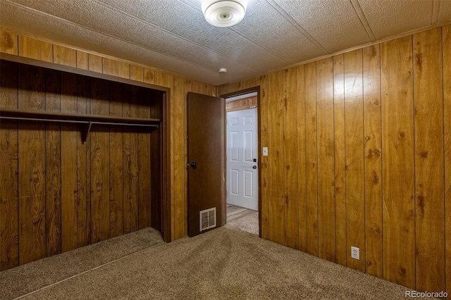 unfurnished bedroom featuring wood walls, a closet, carpet flooring, and visible vents