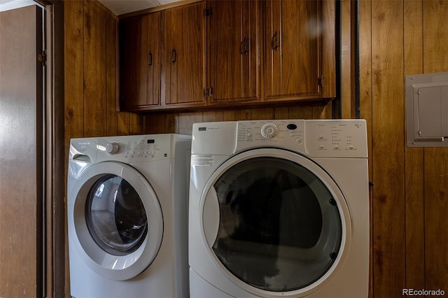 clothes washing area featuring cabinet space, electric panel, wood walls, and independent washer and dryer