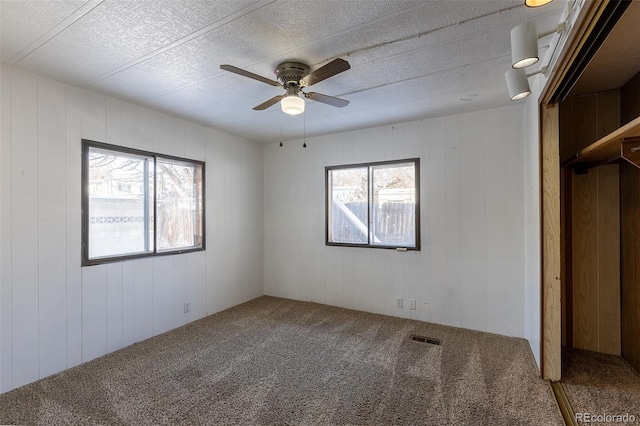 unfurnished bedroom featuring a textured ceiling, multiple windows, carpet, and visible vents