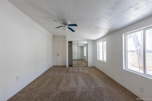 unfurnished bedroom with carpet, lofted ceiling, a closet, a ceiling fan, and a textured ceiling