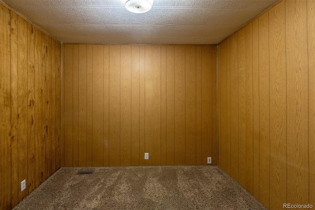 carpeted empty room featuring visible vents and wood walls