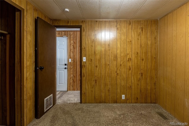 carpeted spare room with visible vents and wooden walls