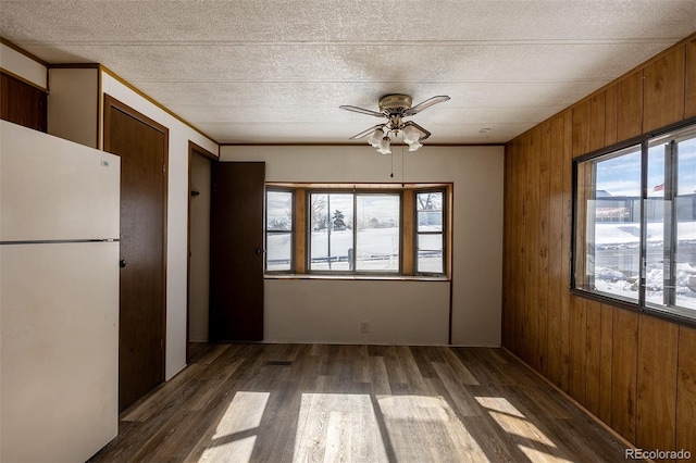 unfurnished dining area featuring ornamental molding, dark wood-style flooring, a ceiling fan, and wooden walls