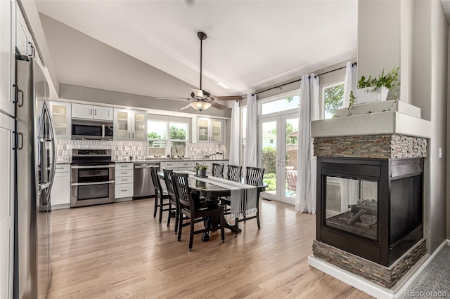 392 Driftwood Cir, Lafayette, CO 80026 - dining space featuring light wood-style flooring, vaulted ceiling, a stone fireplace, ceiling fan, and french doors