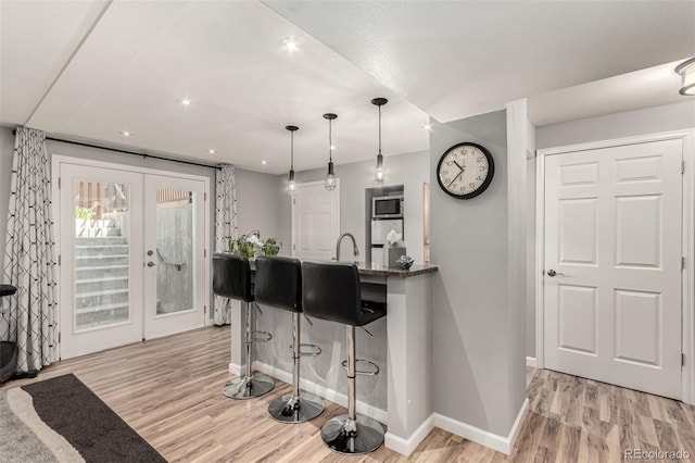 392 Driftwood Cir, Lafayette, CO 80026 - kitchen with stainless steel microwave, french doors, light wood finished floors, a kitchen breakfast bar, and decorative light fixtures