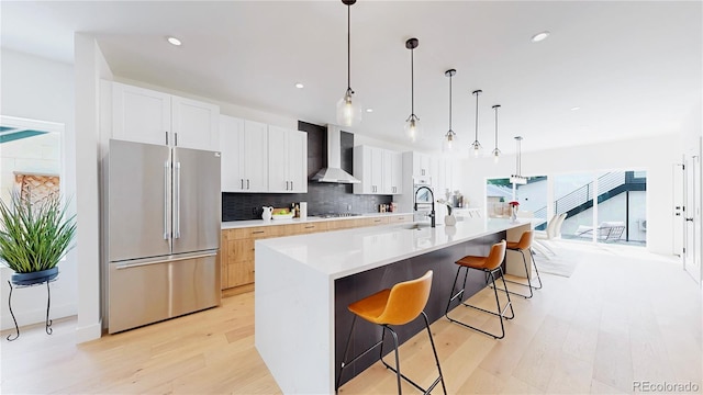 2405 S Franklin, Denver, CO 80210 - kitchen with appliances with stainless steel finishes, wall chimney range hood, light wood finished floors, tasteful backsplash, and white cabinets