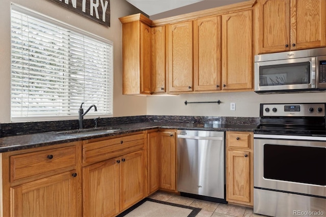 kitchen with light tile patterned floors, appliances with stainless steel finishes, sink, and dark stone countertops