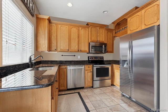 kitchen with appliances with stainless steel finishes, sink, light tile patterned floors, and dark stone counters