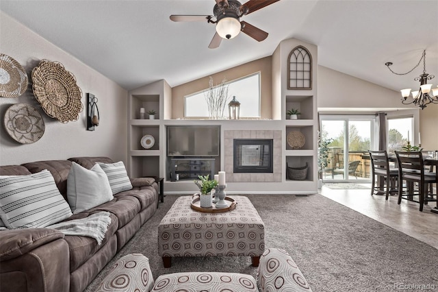 living area with vaulted ceiling, a chandelier, ceiling fan, built in shelves, and a tile fireplace