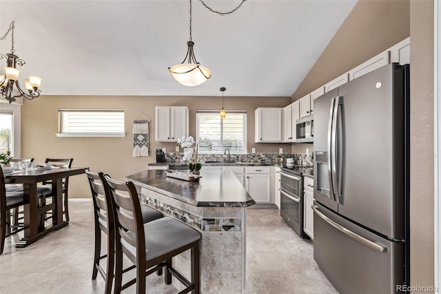 kitchen featuring appliances with stainless steel finishes, dark countertops, a sink, a chandelier, and white cabinetry