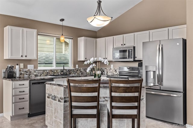 kitchen featuring stainless steel appliances, a sink, white cabinetry, decorative light fixtures, and vaulted ceiling