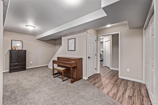 finished below grade area with a textured ceiling, baseboards, wood finished floors, and carpet