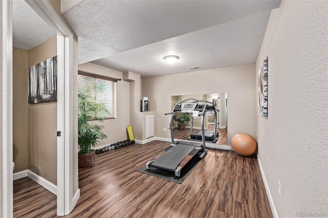 workout area featuring baseboards, wood finished floors, a textured ceiling, and a textured wall