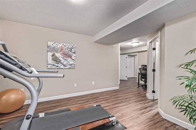 exercise room featuring baseboards, wood finished floors, and a textured ceiling