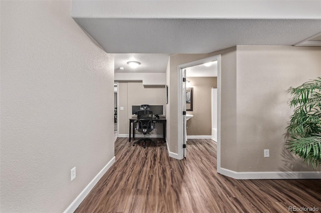 hallway with dark wood-type flooring, an office area, baseboards, and a textured wall