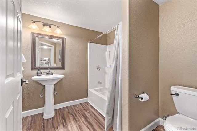 bathroom with wood finished floors, toilet, a textured wall, baseboards, and shower / tub combo with curtain