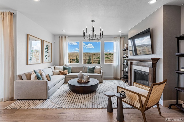 living room featuring a textured ceiling, an inviting chandelier, light hardwood / wood-style flooring, and a tiled fireplace