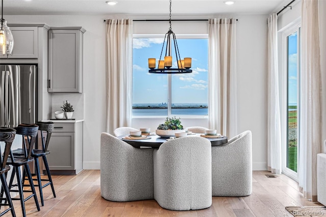 dining space with plenty of natural light, a water view, light hardwood / wood-style floors, and an inviting chandelier