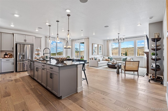 kitchen with gray cabinets, a center island with sink, stainless steel appliances, and light hardwood / wood-style floors