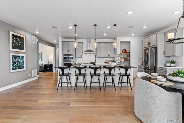 kitchen with gray cabinets, light wood-type flooring, wall chimney range hood, and stainless steel appliances