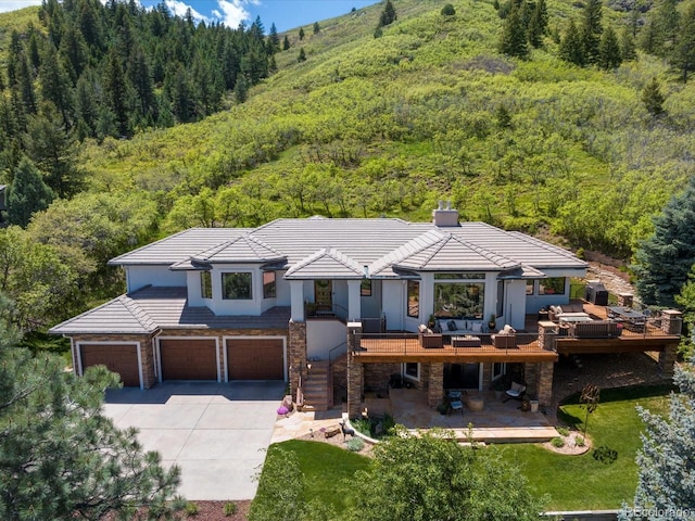 6405 Warriors Run, Littleton, CO 80125 - view of front facade with a view of trees, stone siding, a garage, driveway, and a deck