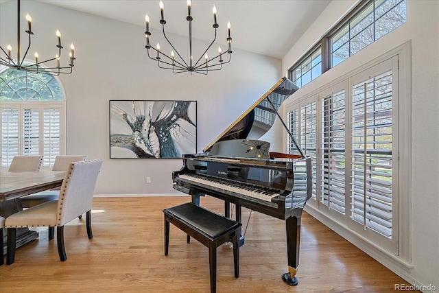living area with baseboards, light wood finished floors, high vaulted ceiling, and an inviting chandelier
