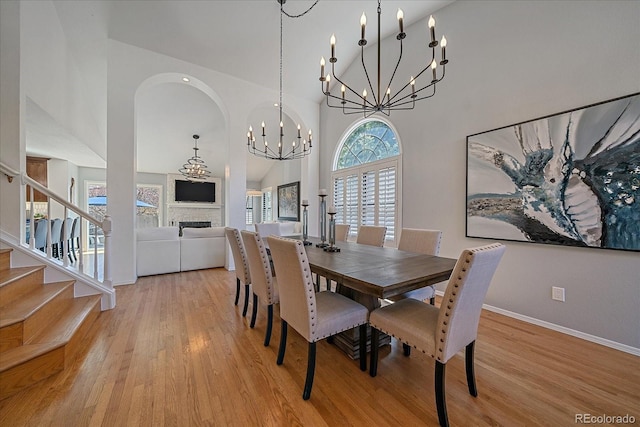 dining space with light wood-style floors, high vaulted ceiling, a fireplace, and an inviting chandelier