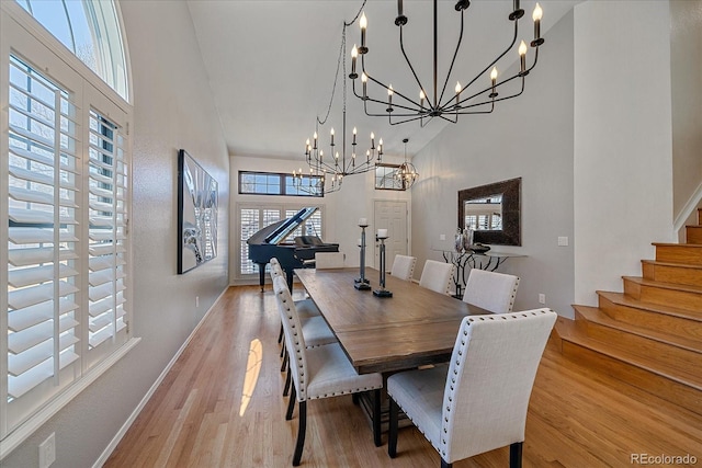 dining area featuring stairway, light wood-type flooring, an inviting chandelier, and a towering ceiling