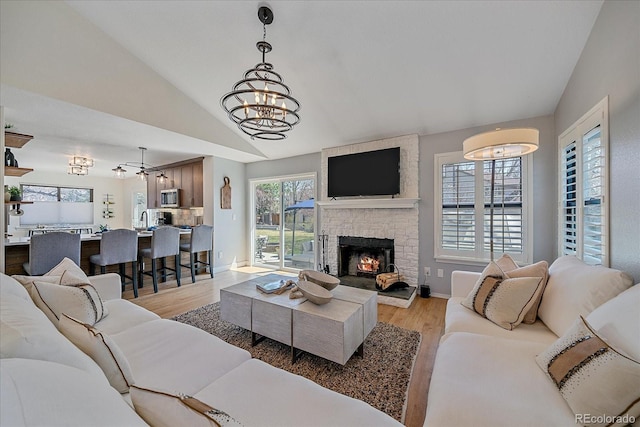 living room featuring baseboards, light wood-type flooring, an inviting chandelier, a fireplace, and lofted ceiling