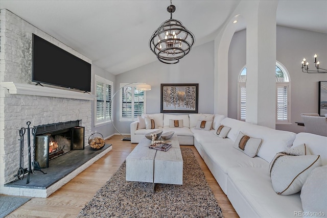 living room with a chandelier, wood finished floors, a fireplace, and vaulted ceiling