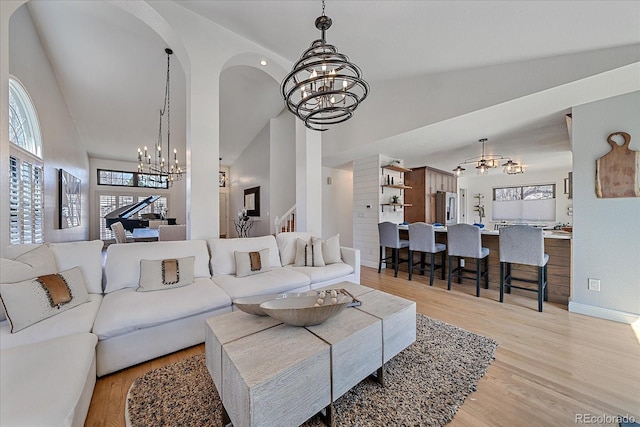 living room with light wood-style floors, high vaulted ceiling, an inviting chandelier, stairway, and baseboards