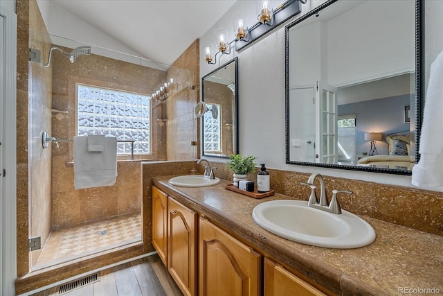 ensuite bathroom with a tile shower, a sink, lofted ceiling, and connected bathroom