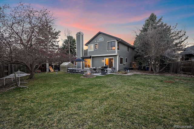 rear view of property with a yard, a fenced backyard, a patio, a fire pit, and a chimney