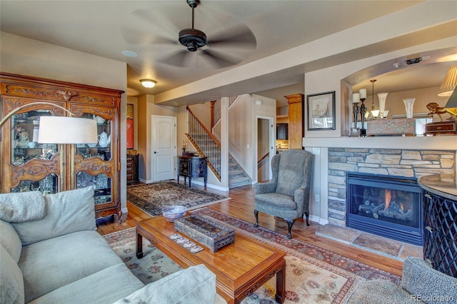 living room with ceiling fan with notable chandelier, a fireplace, and light wood-type flooring