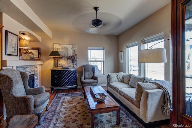 living room featuring ceiling fan, dark wood-type flooring, and a stone fireplace