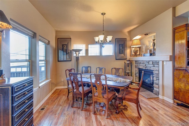 dining room with a stone fireplace, a chandelier, and light hardwood / wood-style flooring