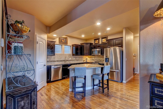 kitchen featuring stainless steel appliances, light wood-type flooring, decorative backsplash, dark brown cabinets, and a kitchen island