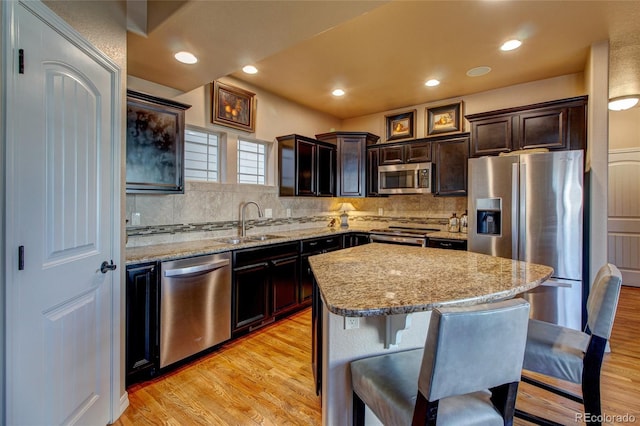 kitchen featuring light stone countertops, a kitchen island, backsplash, appliances with stainless steel finishes, and sink