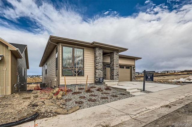 view of front facade with a garage, concrete driveway, stone siding, and central air condition unit