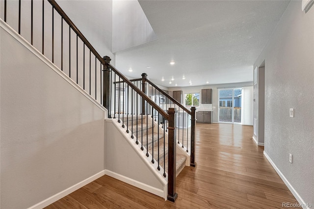 stairway featuring recessed lighting, baseboards, a textured wall, and hardwood / wood-style floors