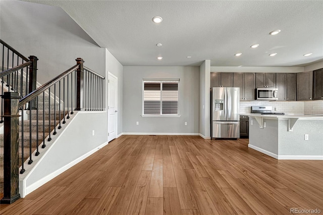 kitchen with dark brown cabinetry, wood finished floors, light countertops, appliances with stainless steel finishes, and a kitchen bar