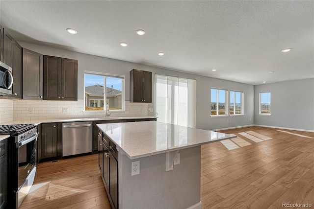 kitchen featuring appliances with stainless steel finishes, light wood-type flooring, decorative backsplash, a center island, and plenty of natural light