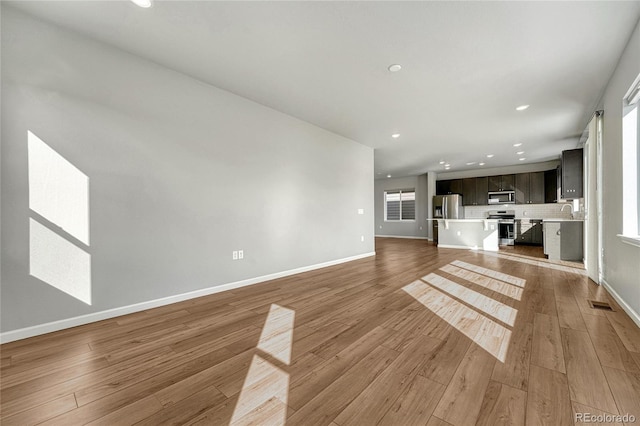 unfurnished living room with visible vents, a sink, light wood-style flooring, and baseboards