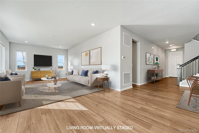 living room featuring light wood finished floors, stairway, visible vents, and baseboards