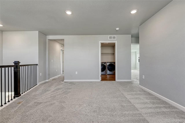 carpeted spare room featuring baseboards, a textured ceiling, visible vents, and washer and dryer