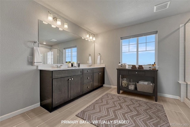 bathroom featuring visible vents, walk in shower, baseboards, and double vanity