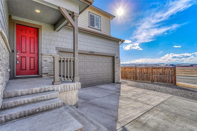 property entrance featuring a garage, concrete driveway, stone siding, and fence