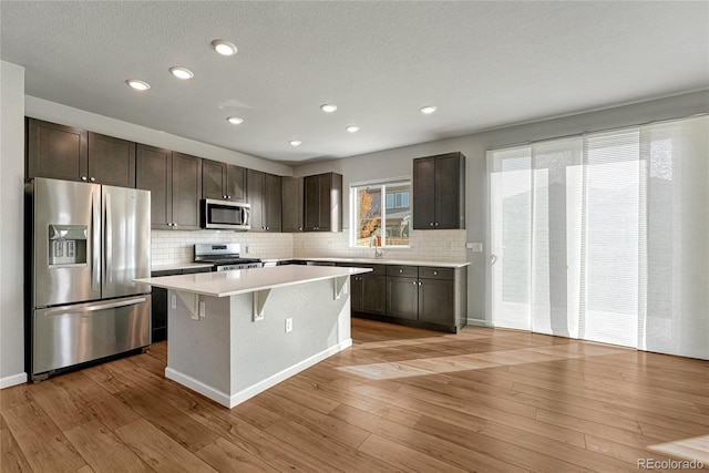 kitchen with dark brown cabinetry, a kitchen island, stainless steel appliances, light countertops, and light wood-type flooring